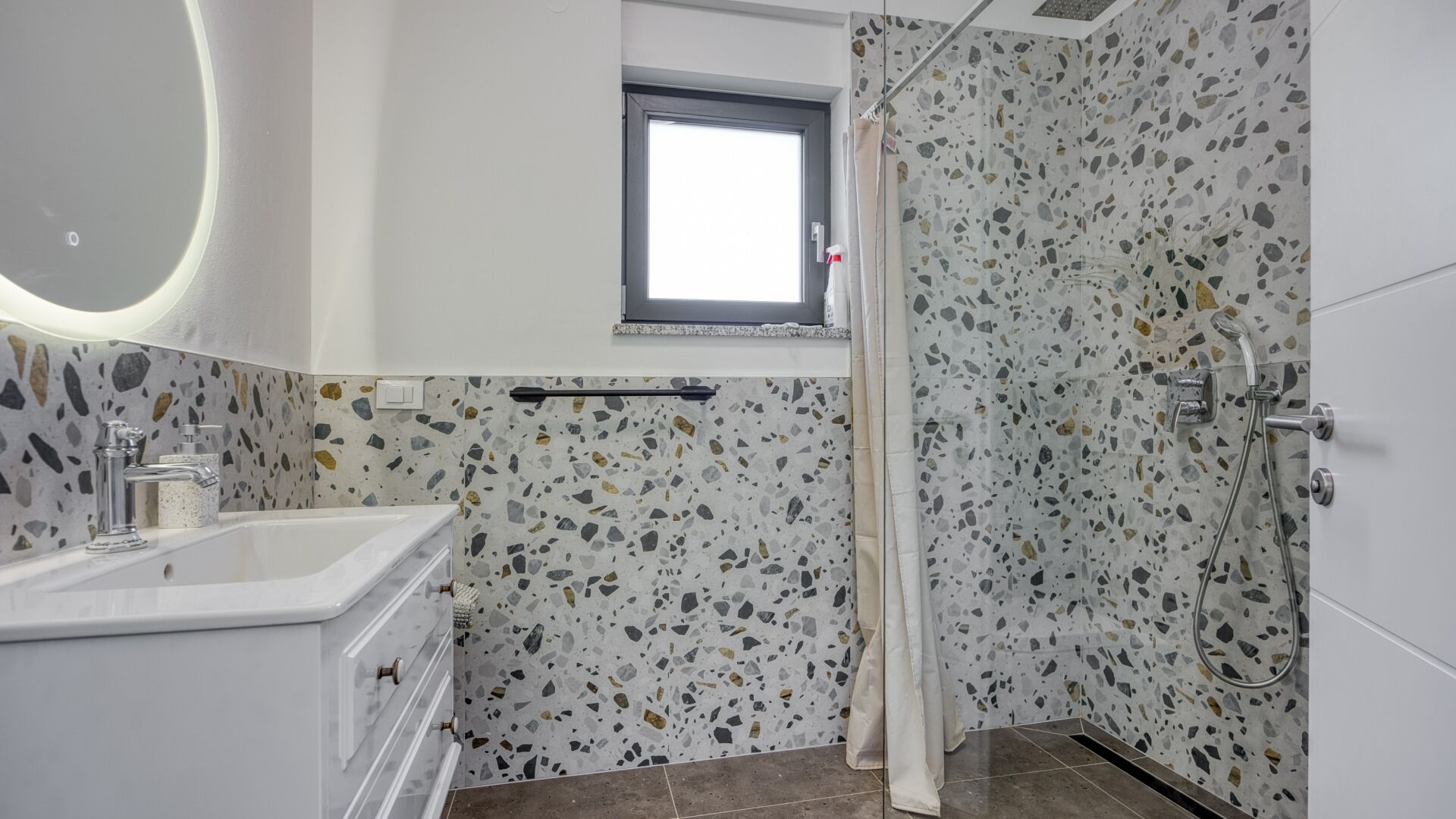 A bathroom with a white sink, a mirror, a shower with a glass door, and terrazzo flooring.