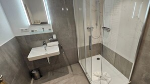 Un bany modern amb dutxa trencada per vidre, un rentapins blanc i un mirall a sobre.