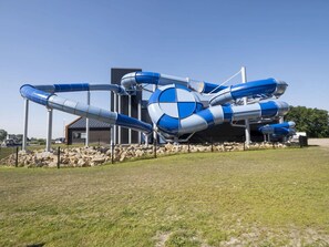 A large water slide structure with multiple lanes, a building in the background, and a fenced area with grass.