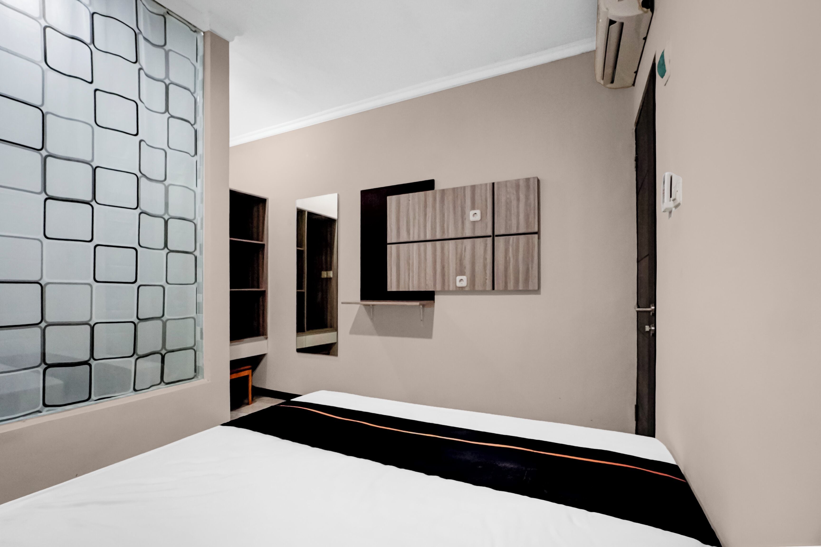 A bedroom with a bed, a wardrobe, a mirror, and a wall-mounted air conditioning unit.