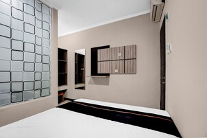 A bedroom with a bed, a wardrobe, a mirror, and a wall-mounted air conditioning unit.