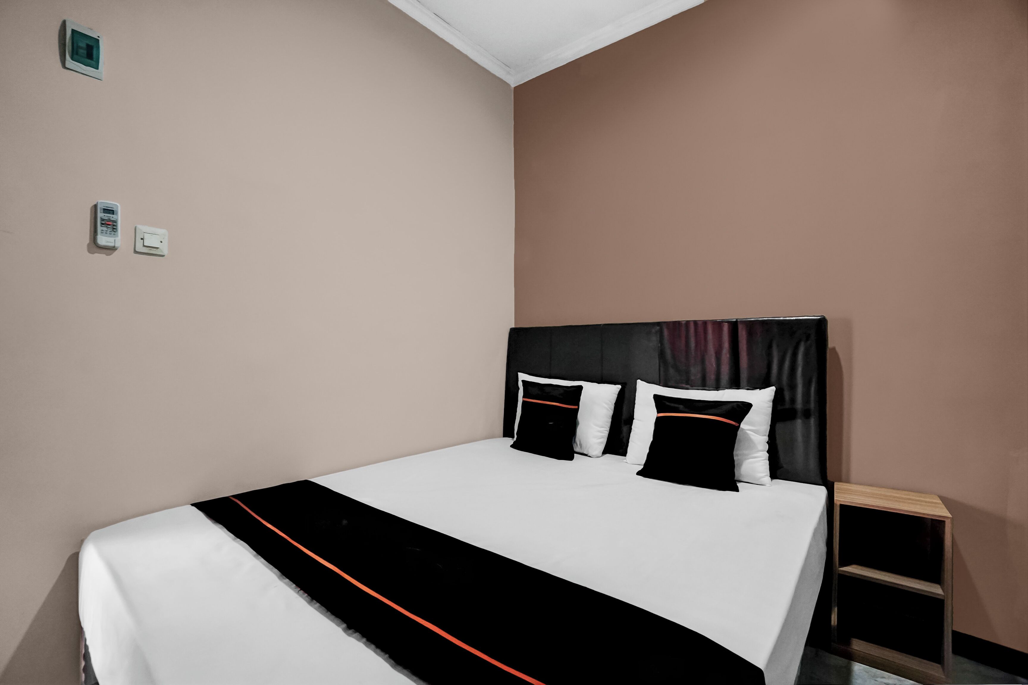 A neatly made bed with a black and white bedspread, a headboard with a black and white pattern, and a small bedside table with a lamp.