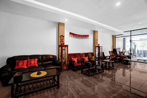 A modern living room with a leather sofa, wooden coffee table, and traditional chairs. A red banner with text is visible on the wall.