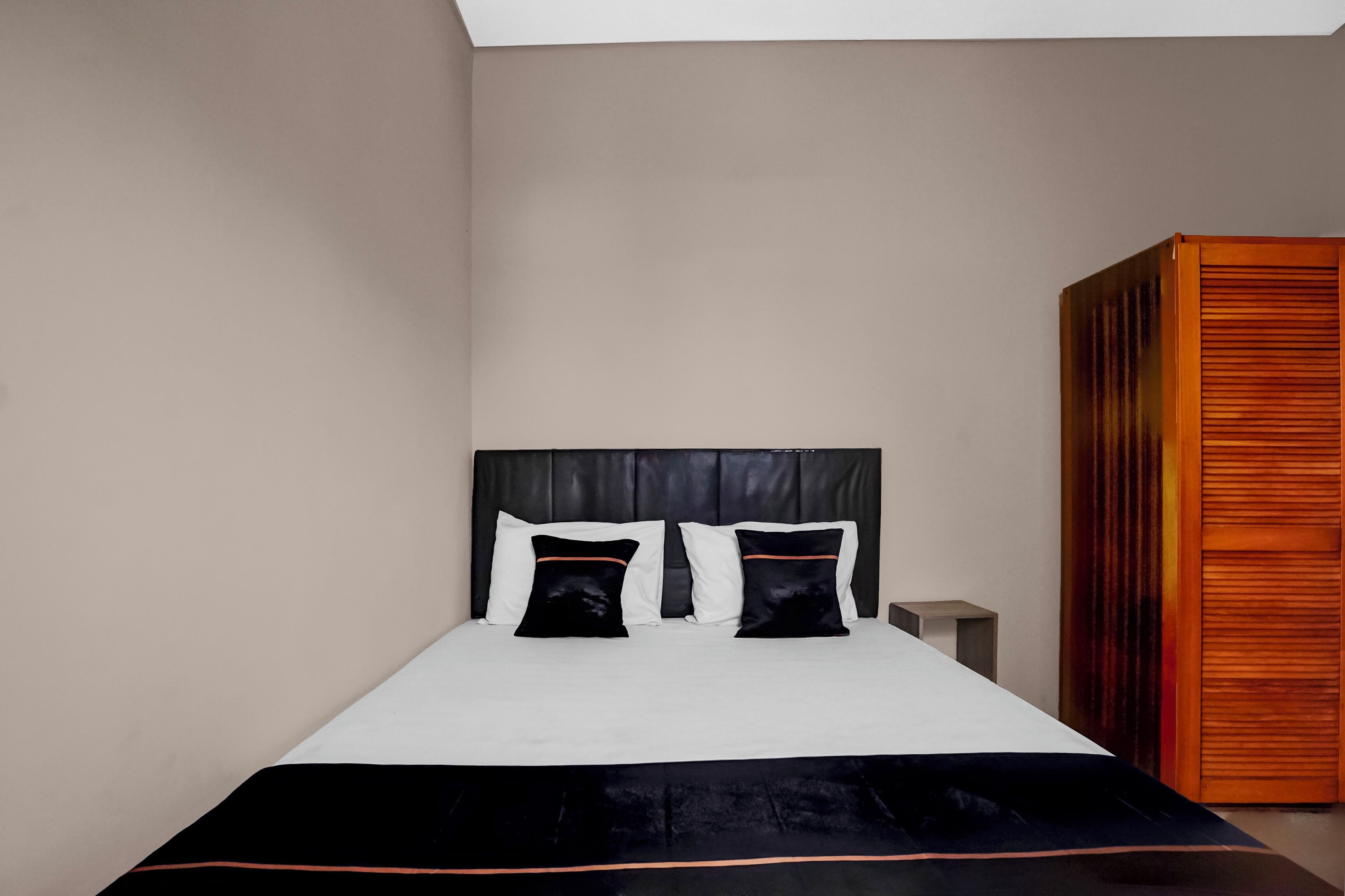 A modern bedroom with a large bed, a wooden wardrobe, and a nightstand.