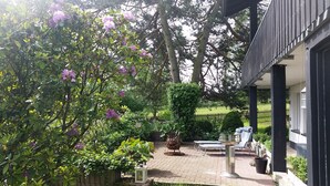 A patio area with a brick floor, outdoor furniture, and a garden with trees and shrubs. - Apartment Gartenblick, 96 sqm, 2 Bedrooms, Max. 4 Guests (Balve)