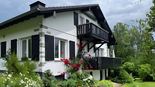 A two-story house with a balcony, stone steps, and a variety of plants. - Apartment Gartenblick, 96 sqm, 2 Bedrooms, Max. 4 Guests (Balve)