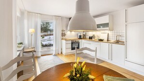 A modern kitchen with white cabinets, a wooden dining table, and a hanging pendant light. - Apartment Gartenblick, 96 sqm, 2 Bedrooms, Max. 4 Guests (Balve)
