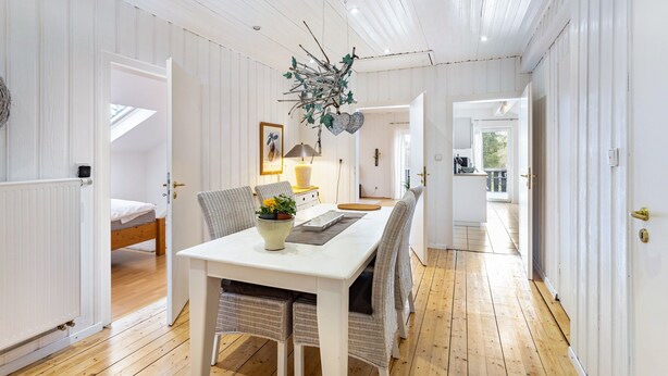 A room with a white dining table, wicker chairs, a hanging branch decoration, and a view to a balcony. - Apartment Weitblick, 106 sqm, 3 bedrooms, max. 5 guests (Balve)