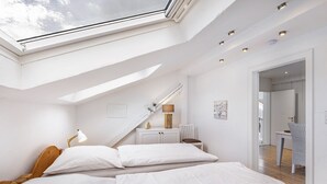 A bedroom with a skylight, a bed with white linens, a desk with a lamp, and a chair. - Apartment Weitblick, 106 sqm, 3 bedrooms, max. 5 guests (Balve)