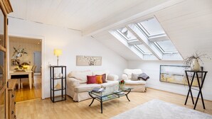 A spacious loft with a high ceiling, skylights, a white sofa, a glass coffee table, and a dining area with a lamp. - Apartment Weitblick, 106 sqm, 3 bedrooms, max. 5 guests (Balve)