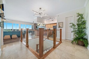 A spacious living area with a glass railing, a chandelier, and a large window overlooking a balcony. - Sailmakers Place 903 | Two-Story Penthouse | Panoramic Views | My Beach Getaways (Pensacola)