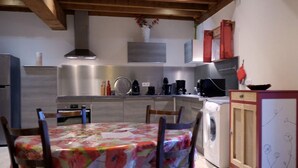 A kitchen with a dining table covered in a floral tablecloth, a washing machine, and a cabinet with a floral design.