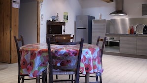 A dining area with a table covered in a floral tablecloth, wooden chairs, and a wooden ceiling with exposed beams.