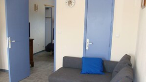 Een woonkamer met een grijze bank, een blauw kussen en een deur naar een andere kamer.