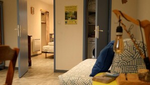 Een hotelkamer met een bed, een stoel, een tafel met een lamp, een klok en een poster aan de muur.