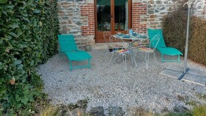 Een terras met een tafel, stoelen, een groene parasol en een stenen muur.