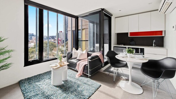 A modern living room with a large window, a black sofa, a white coffee table, and a dining area with black chairs. - Comfy City Apt Beside Queen Victoria Market (Melbourne)
