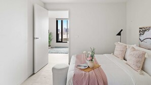A bedroom with a bed, bedside table, and a view of the city through a window. - Comfy City Apt Beside Queen Victoria Market (Melbourne)