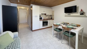 Ein kompakter Wohnbereich mit Küchenzeile, Essbereich und Wand-Fernseher.