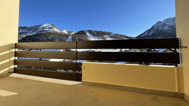 Ein Balkon mit Holzgeländer mit Blick auf eine verschneite Berglandschaft.