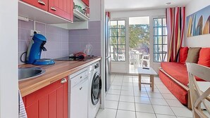 Una cocina compacta con armarios rojos, una cafetera azul y una lavadora.