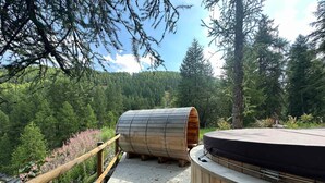 Estructura de sauna de madera con banco, ubicada en una terraza de madera rodeada de bosque.
