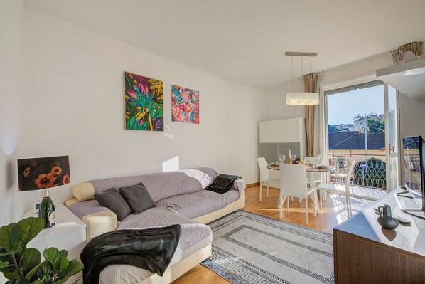 Una sala de estar moderna con un sofá, una mesa de comedor y sillas. Hay dos cuadros en la pared, una lámpara y una planta.