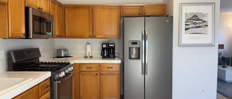 Una cocina con gabinetes de madera, un refrigerador de acero inoxidable, un microondas, una estufa y una cafetera.
