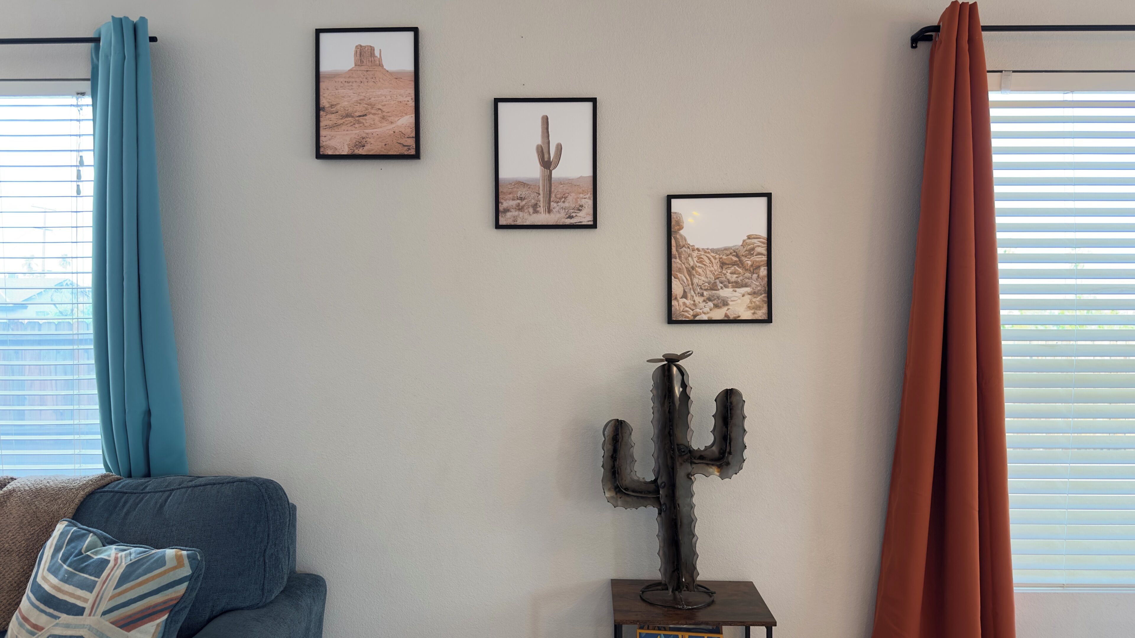 A room with a blue sofa, a cactus sculpture, and three framed pictures on the wall.