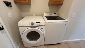 A compact laundry area with a front-loading washing machine and a stacked dryer. - 4BrHome • MountainViews • SolarSetup: EverydayStay (Twentynine Palms)