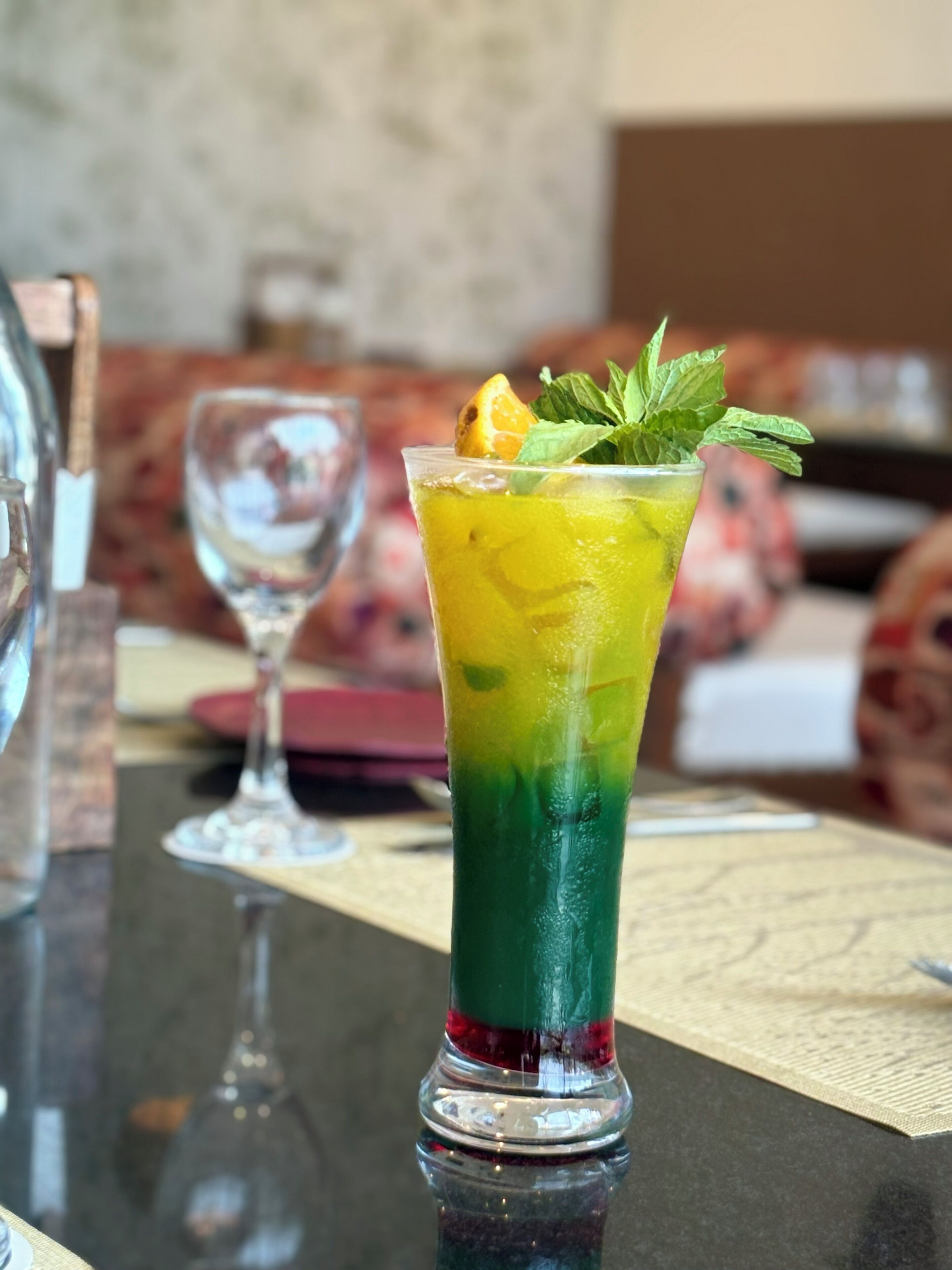 A tall glass with layered drinks, a glass of water, and a bottle on a table.