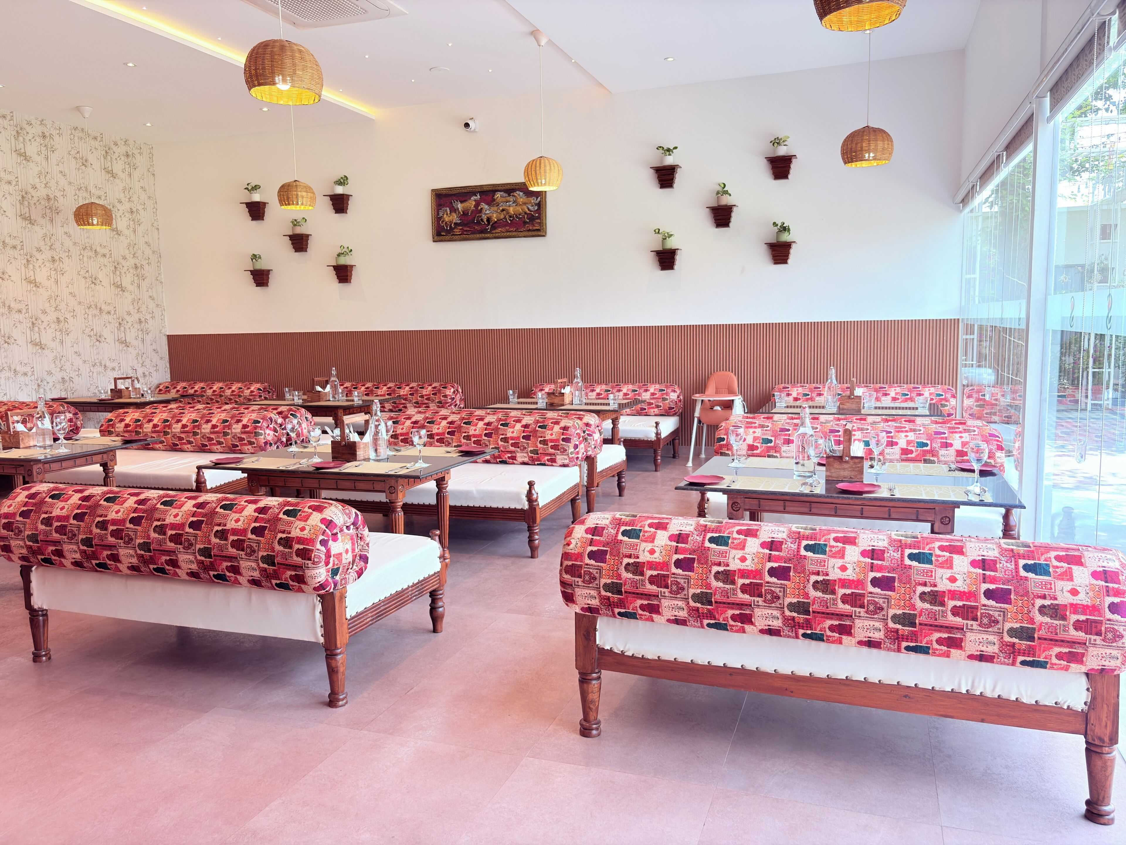 A restaurant with wooden tables and benches, potted plants on the walls, and a large window.