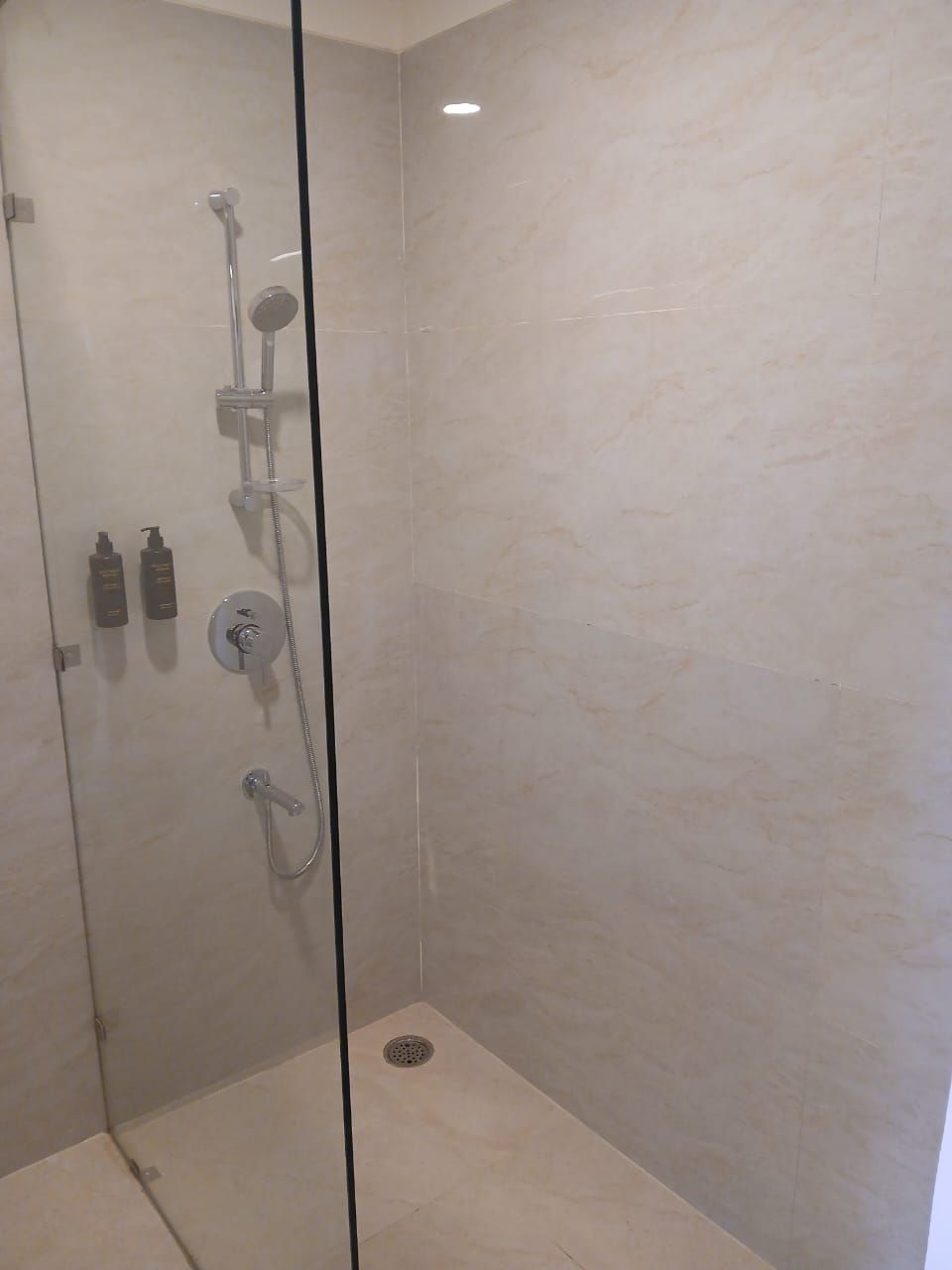 A glass-enclosed shower with a handheld showerhead, a wall-mounted faucet, and a handheld showerhead.