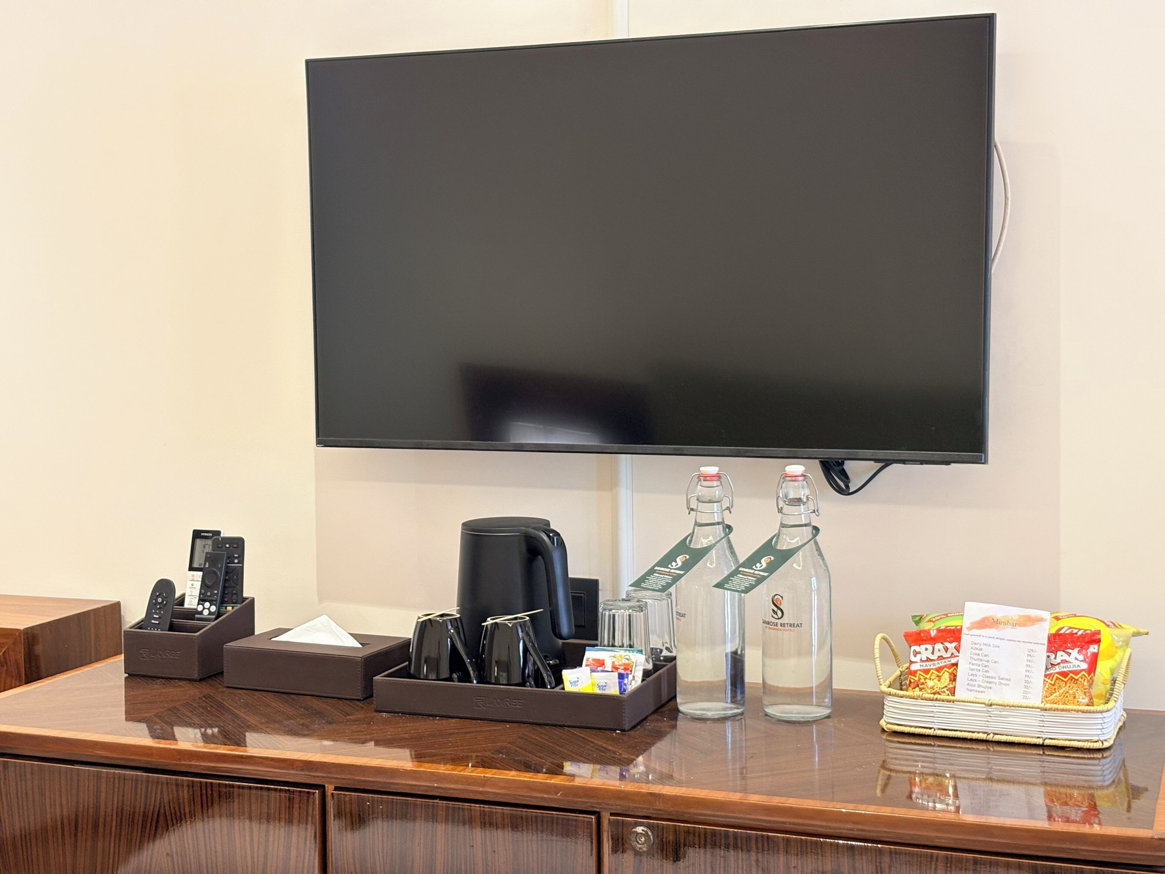 Een hotel receptiebalie met een flatscreen televisie, een koffieapparaat, een drankdispenser, een afstandsbedieninghouder en een mand met snacks.