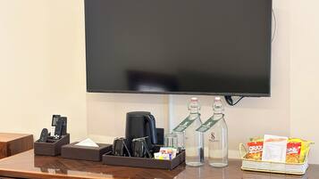 Een hotel receptiebalie met een flatscreen televisie, een koffieapparaat, een drankdispenser, een afstandsbedieninghouder en een mand met snacks.