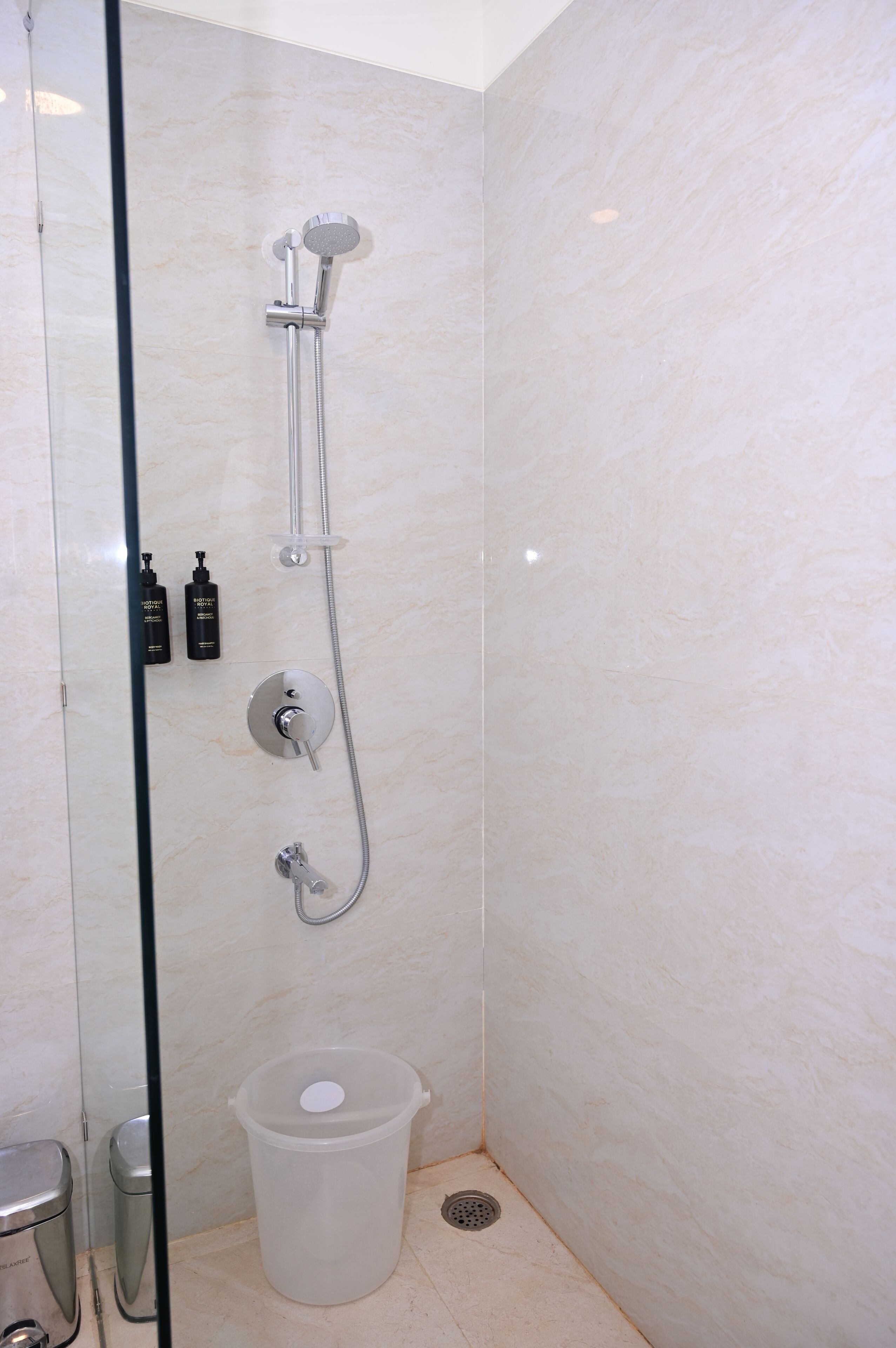 A shower with a handheld showerhead, a wall-mounted faucet, and two bottles of shampoo.