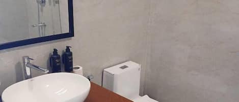 Ein modernes Badezimmer mit einem großen weißen Waschbecken, einem Spiegel, einer Toilette und einer Duschkabine.