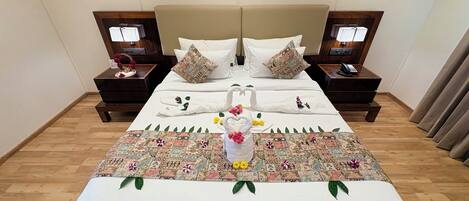 A hotel room with a large bed, two nightstands, a wooden floor, and a decorative bedspread.