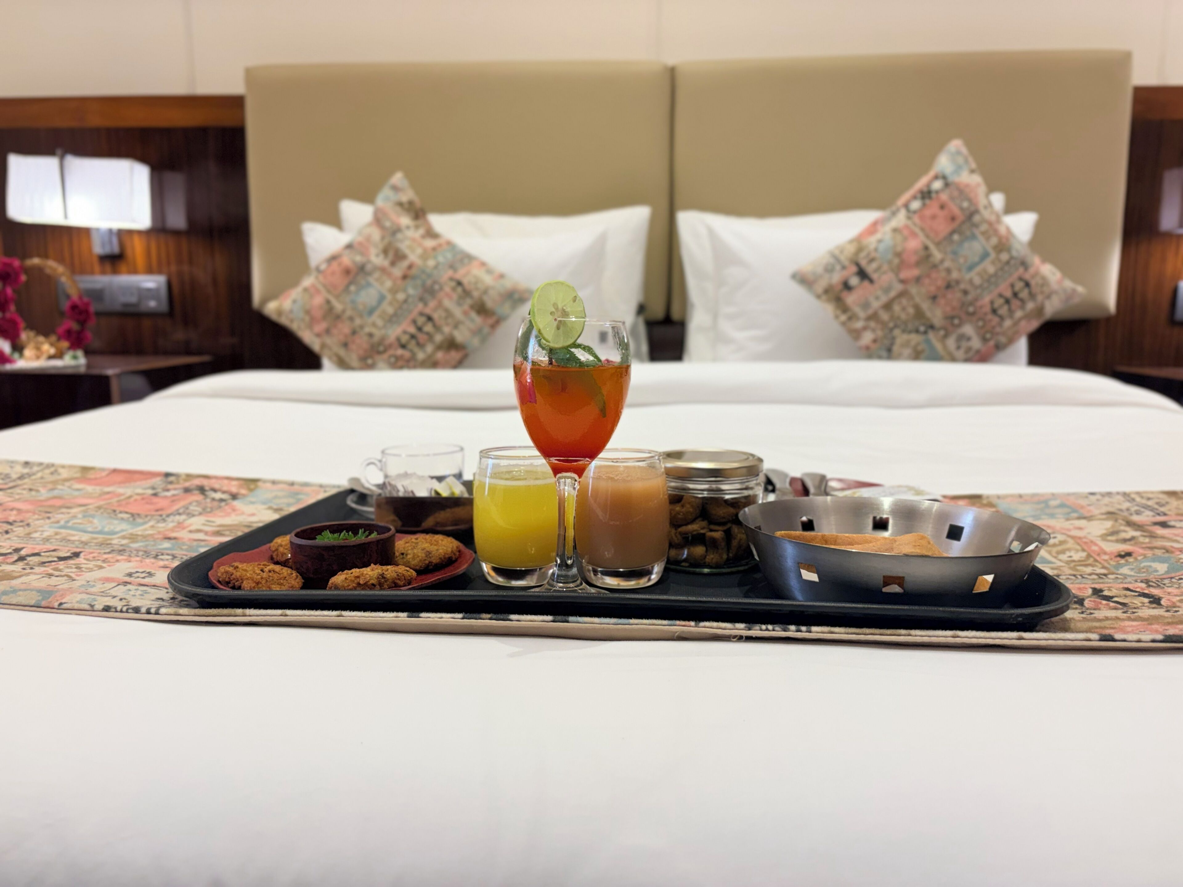 A breakfast tray with various foods and drinks on a bed in a hotel room.