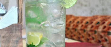 A tall glass with ice, lime slices, and mint leaves, placed on a table with a woven placemat.