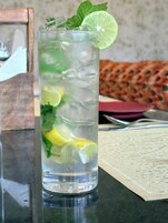 A tall glass with ice, lime slices, and mint leaves, placed on a table with a woven placemat.