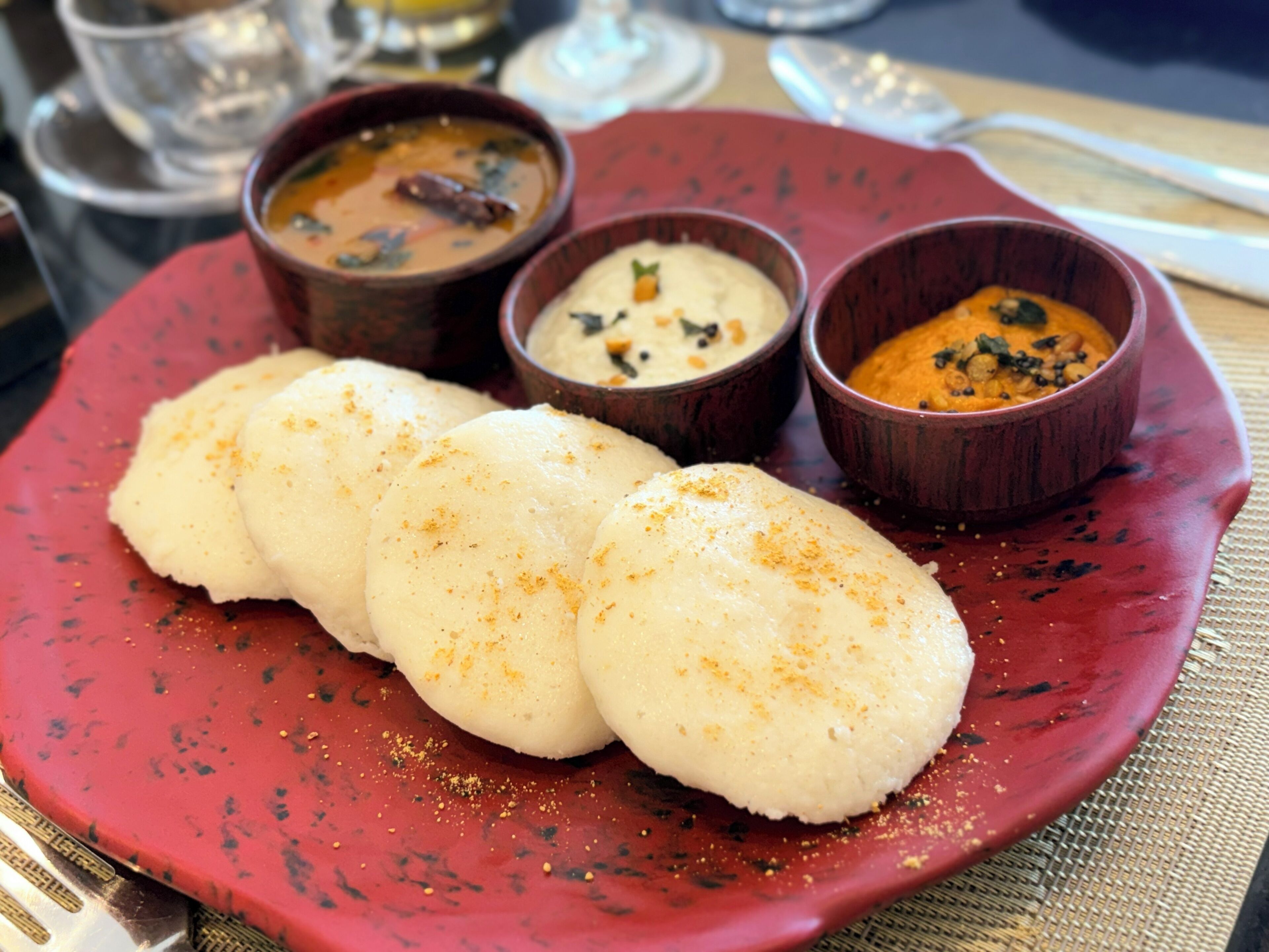A plate with three white dumplings and three small bowls of soup.