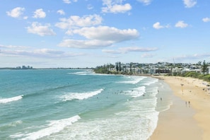 A beach with waves, a sandy shore, and buildings in the background. - Bright Coastal 3BR Apartment Opposite the Beach (Sunshine Coast)