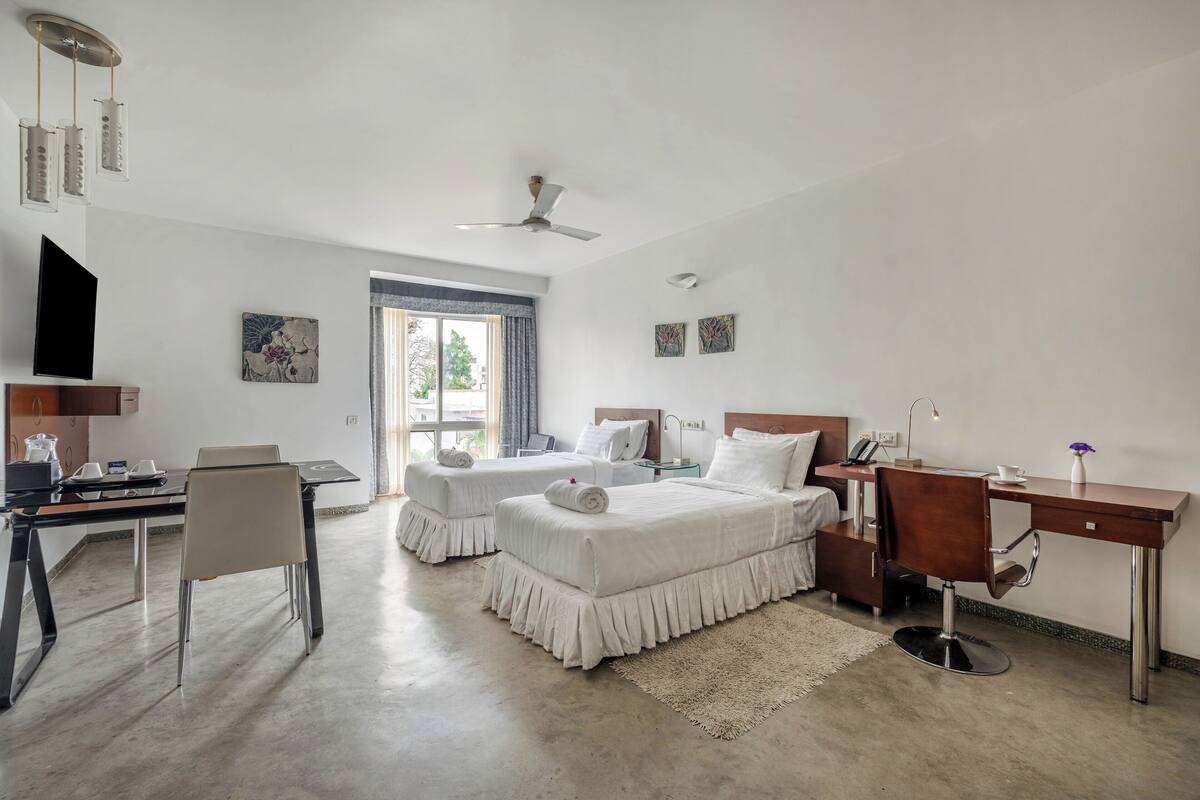 A hotel room with two beds, a desk, a chair, a TV, and a window with a view.