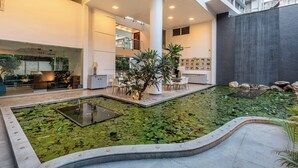 Un jardí interior modern amb un estany, zona de seients i una escala que condueix a un nivell superior.