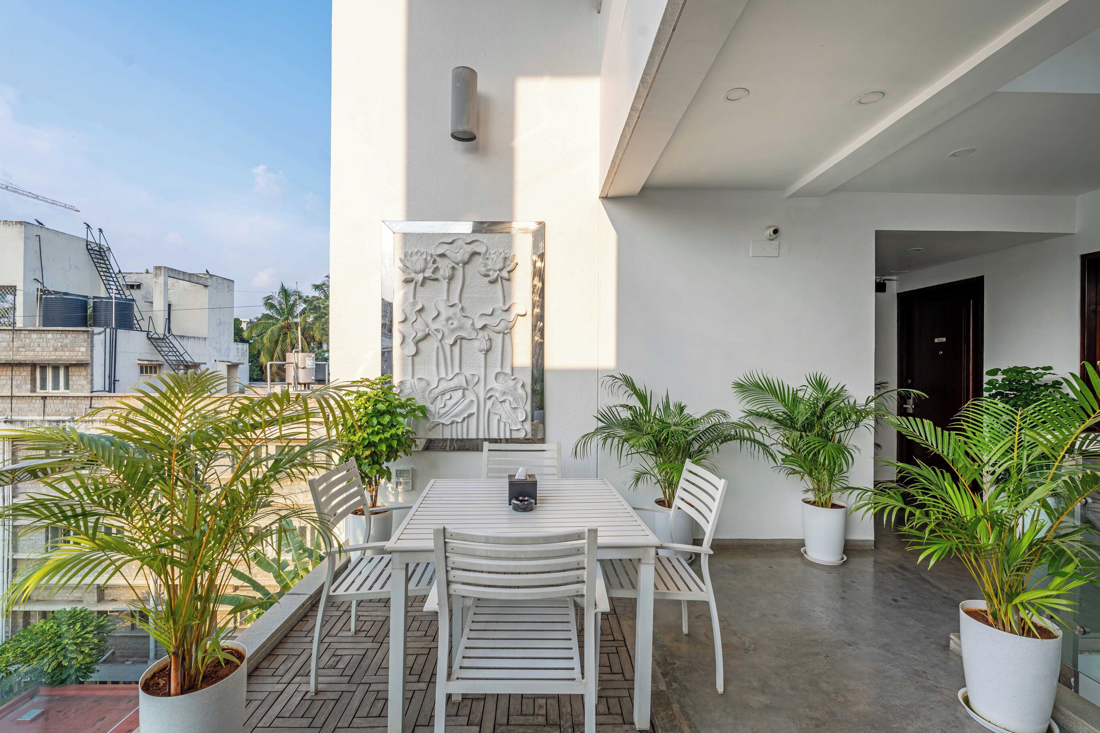 A modern outdoor patio area with a white table and chairs, surrounded by potted plants.