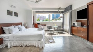 Una habitació d'hotel amb un llit gran, un escriptori, una cadira, un televisor i vista a la ciutat.