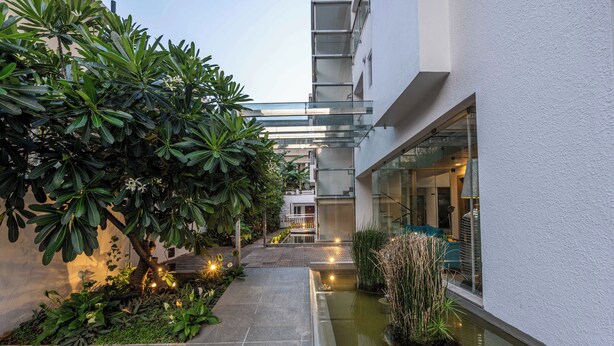 Un edifici modern amb façana de vidre, un petit pati interior amb una font i vegetació abundant.