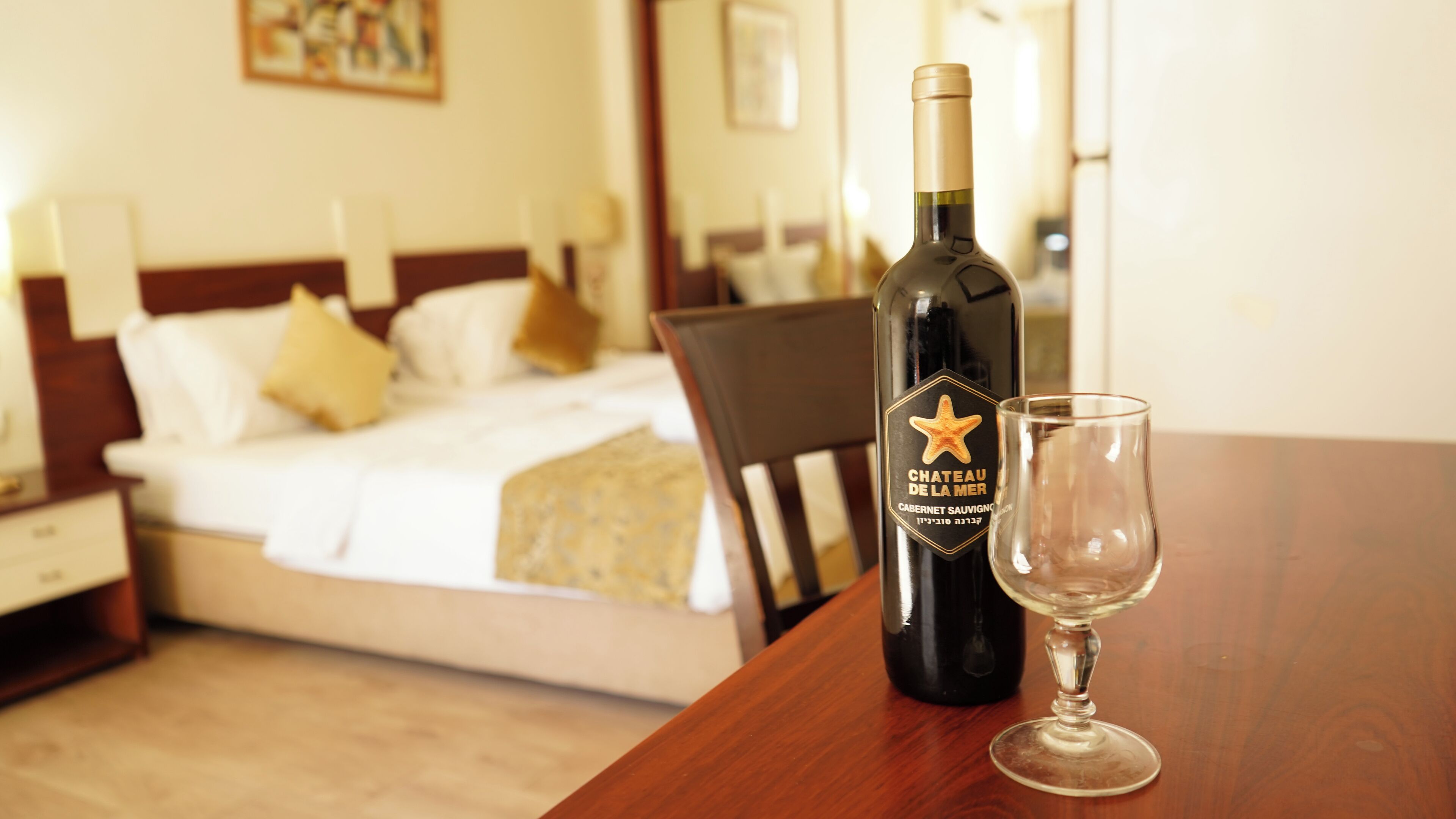 Una botella de vino Chateau de la Mer y una copa sobre una mesa de madera en una habitación de hotel.