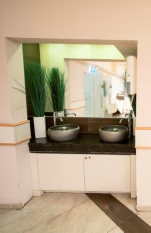A bathroom with two round sinks, a mirror, and a potted plant. - Aristocrat Hotel (Bene Beraq)